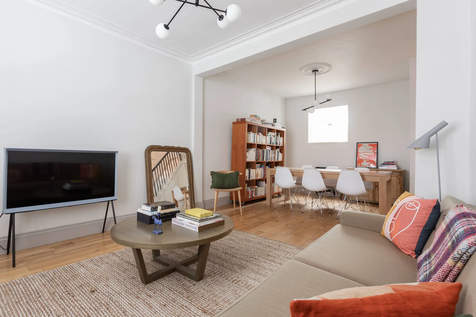 A bright living room opens into a dining area with a table and bookshelves.