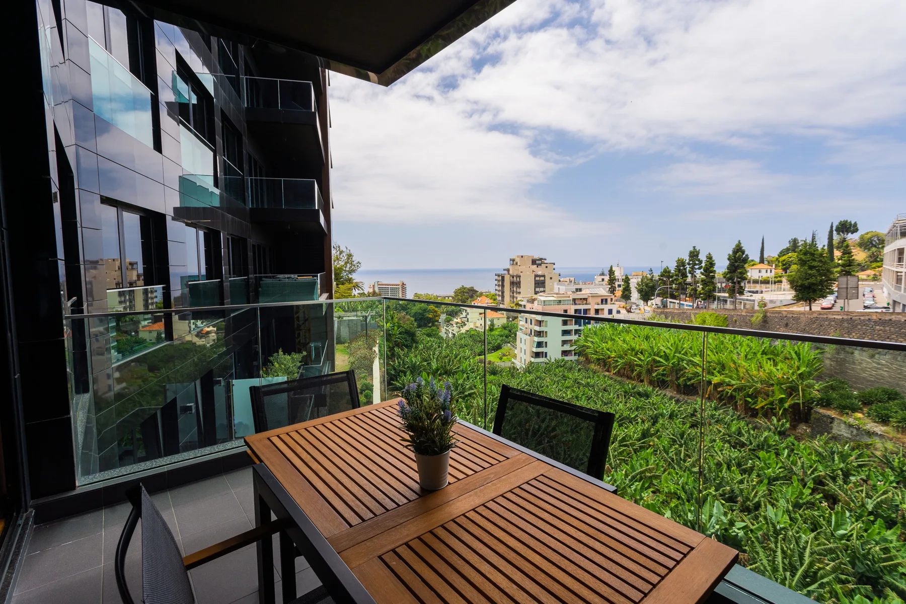 A balcony dining area overlooks lush greenery and a distant ocean view.