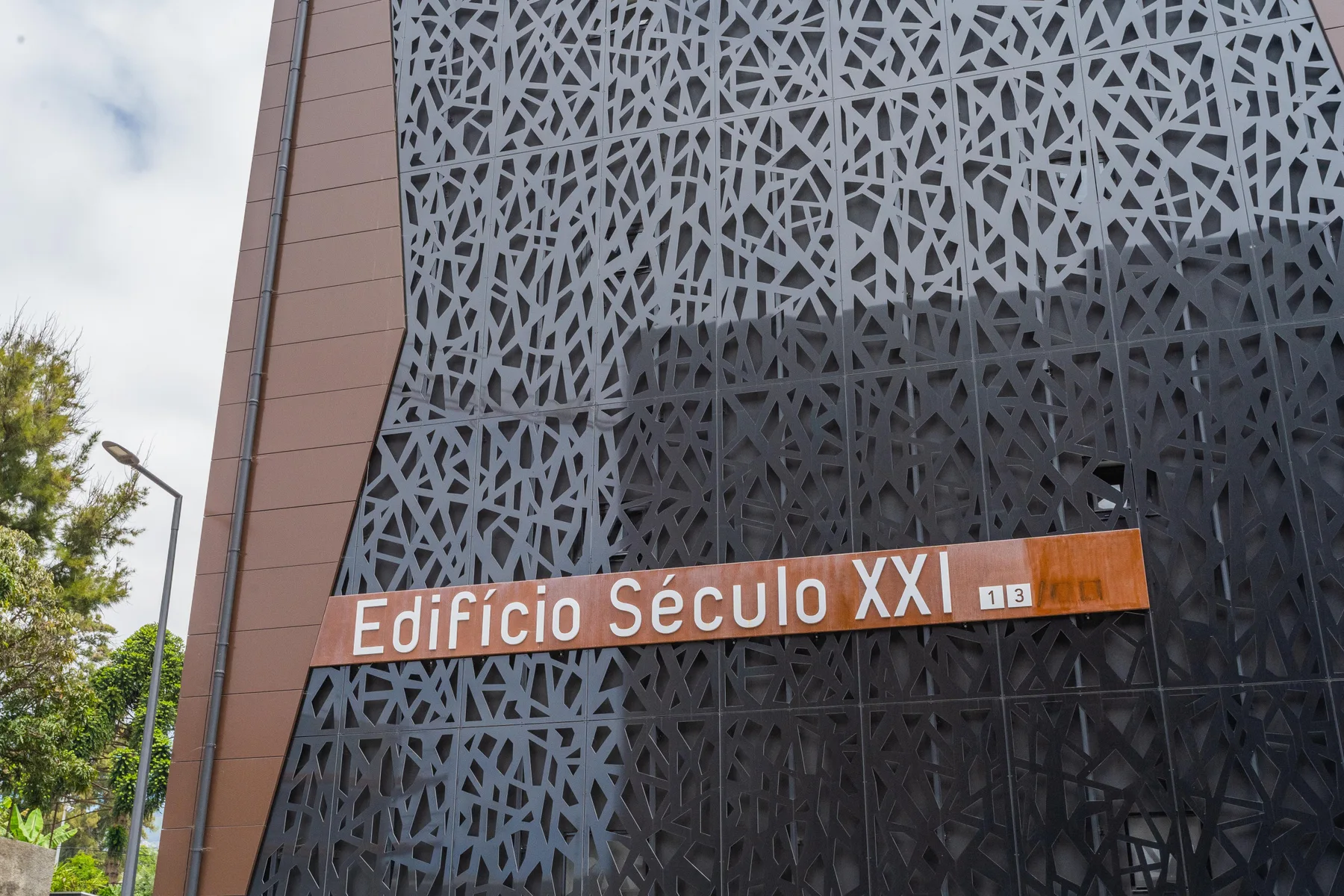 A modern building facade features a dark geometric screen and a sign reading Edifício Século XXI.
