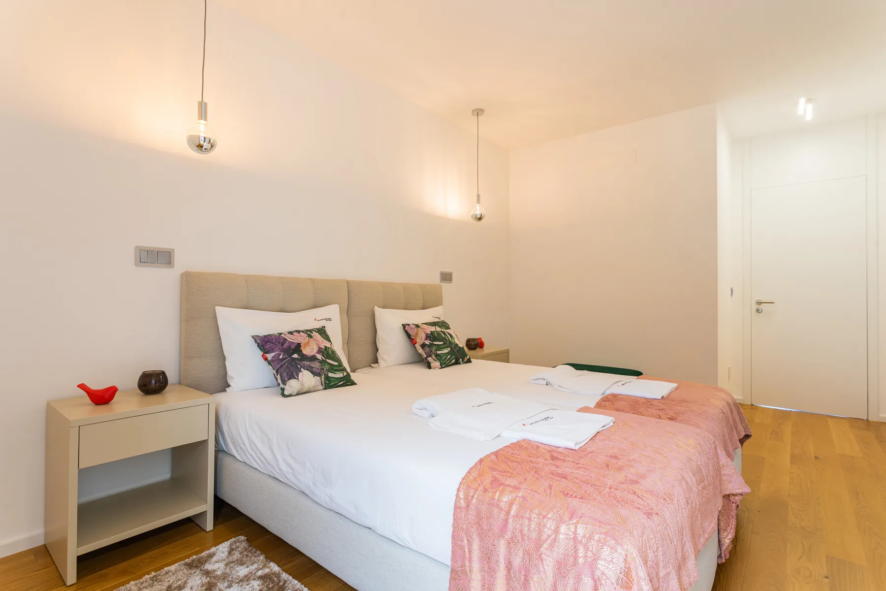 Un dormitorio con dos camas, mesitas de noche y una puerta blanca.