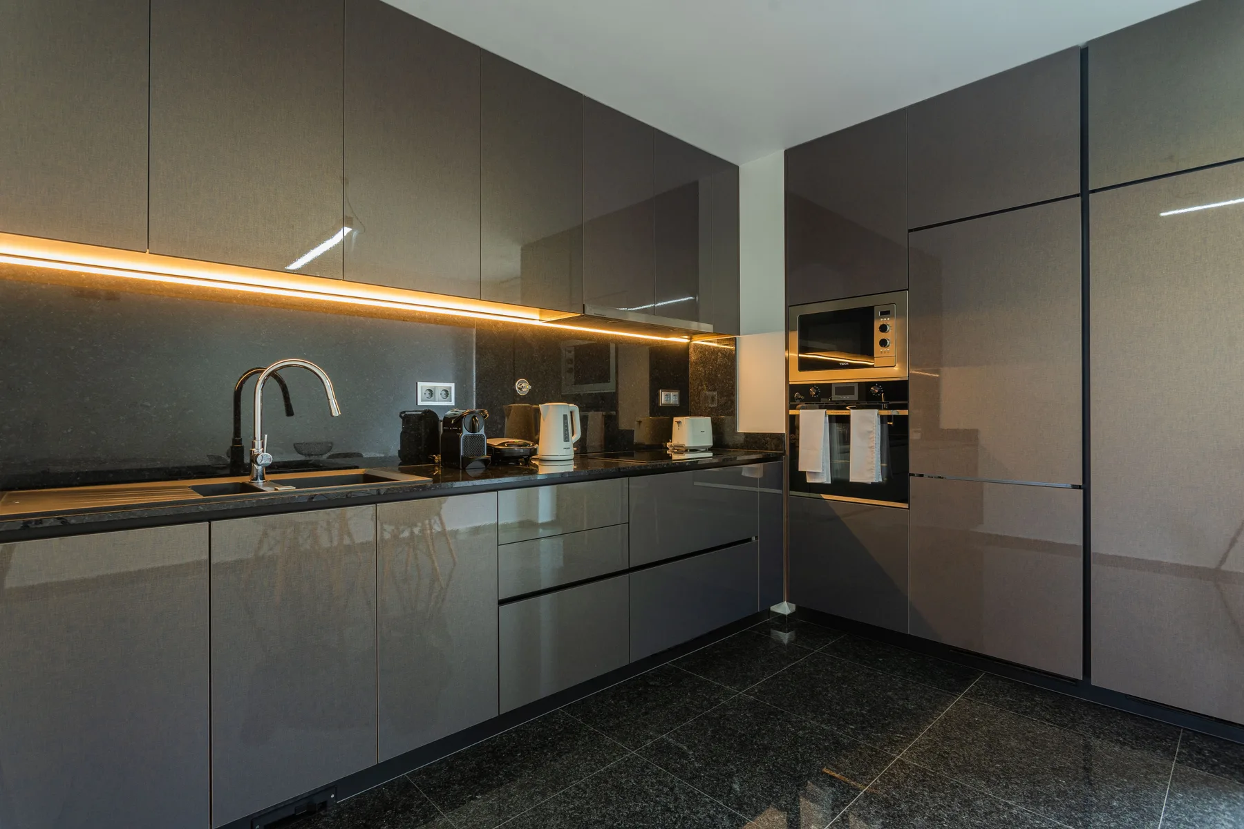 A modern kitchen with dark cabinets, a sink, and built-in appliances.