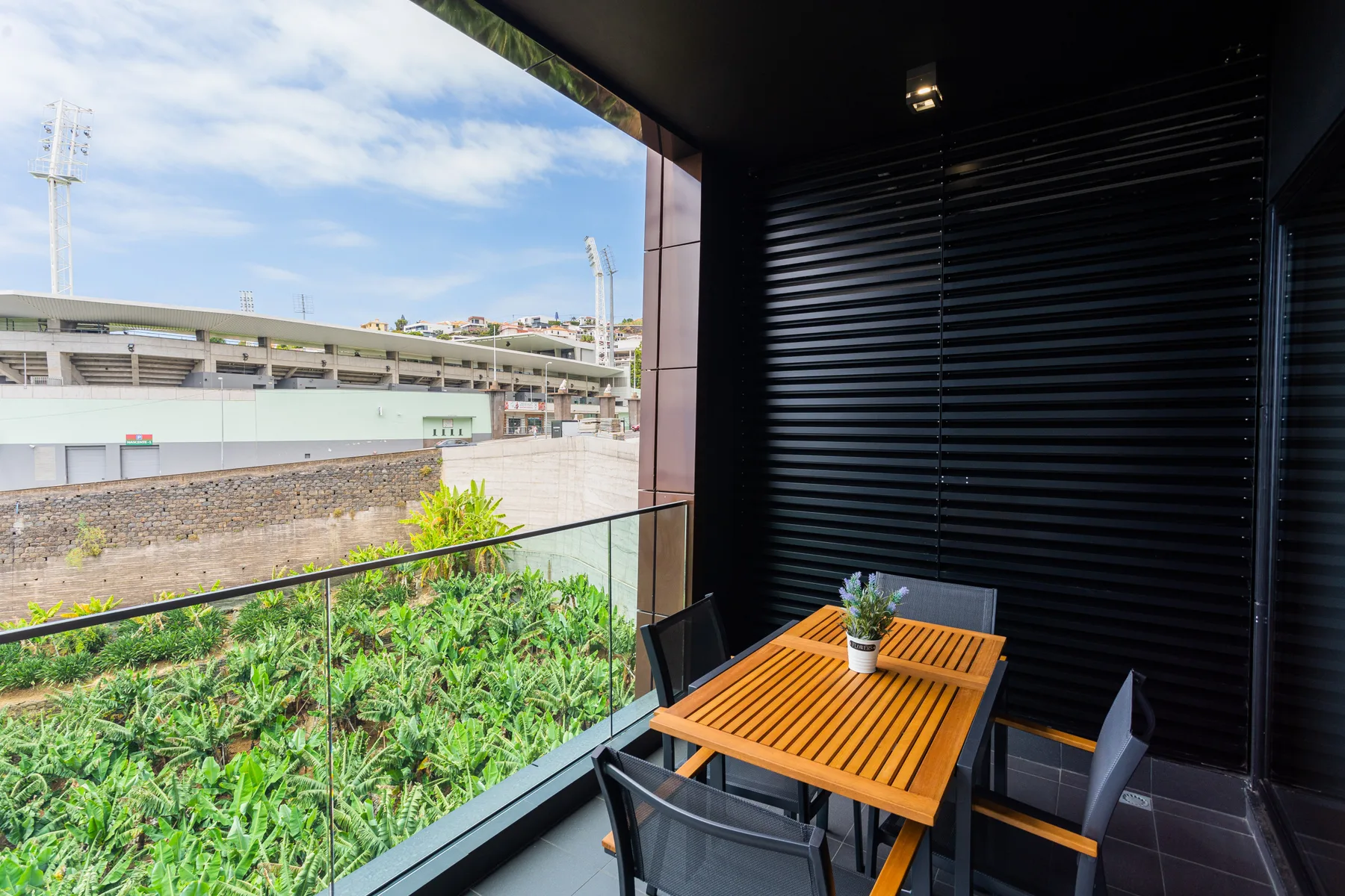 A covered balcony has a wooden table and seating beside a glass railing.