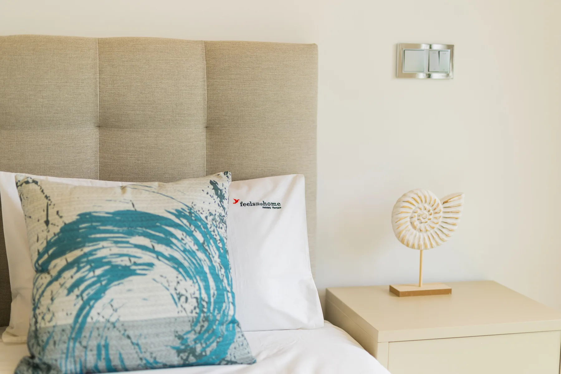Un dormitorio con una cama, un cojín estampado en tonos turquesa y una mesita de noche.