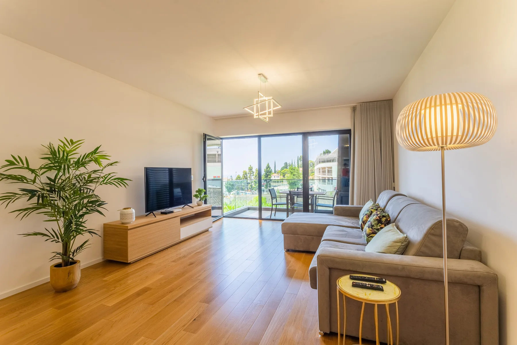 A bright living room with seating, a television, and glass doors opening onto a balcony.