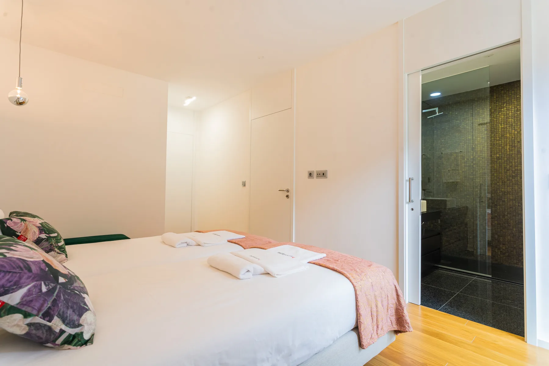 A bright bedroom with a neatly made bed beside an open bathroom doorway.