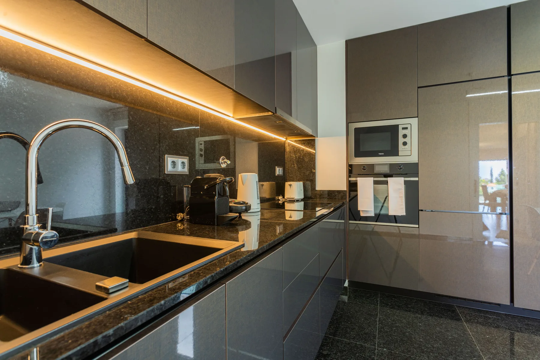 A modern kitchen with dark countertops, cabinets, and built-in appliances.
