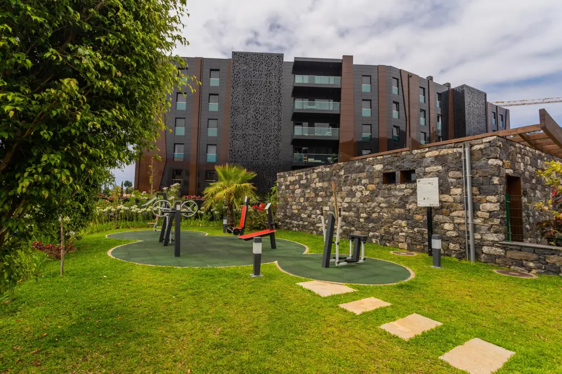 A landscaped outdoor exercise area with fitness equipment beside a stone wall.