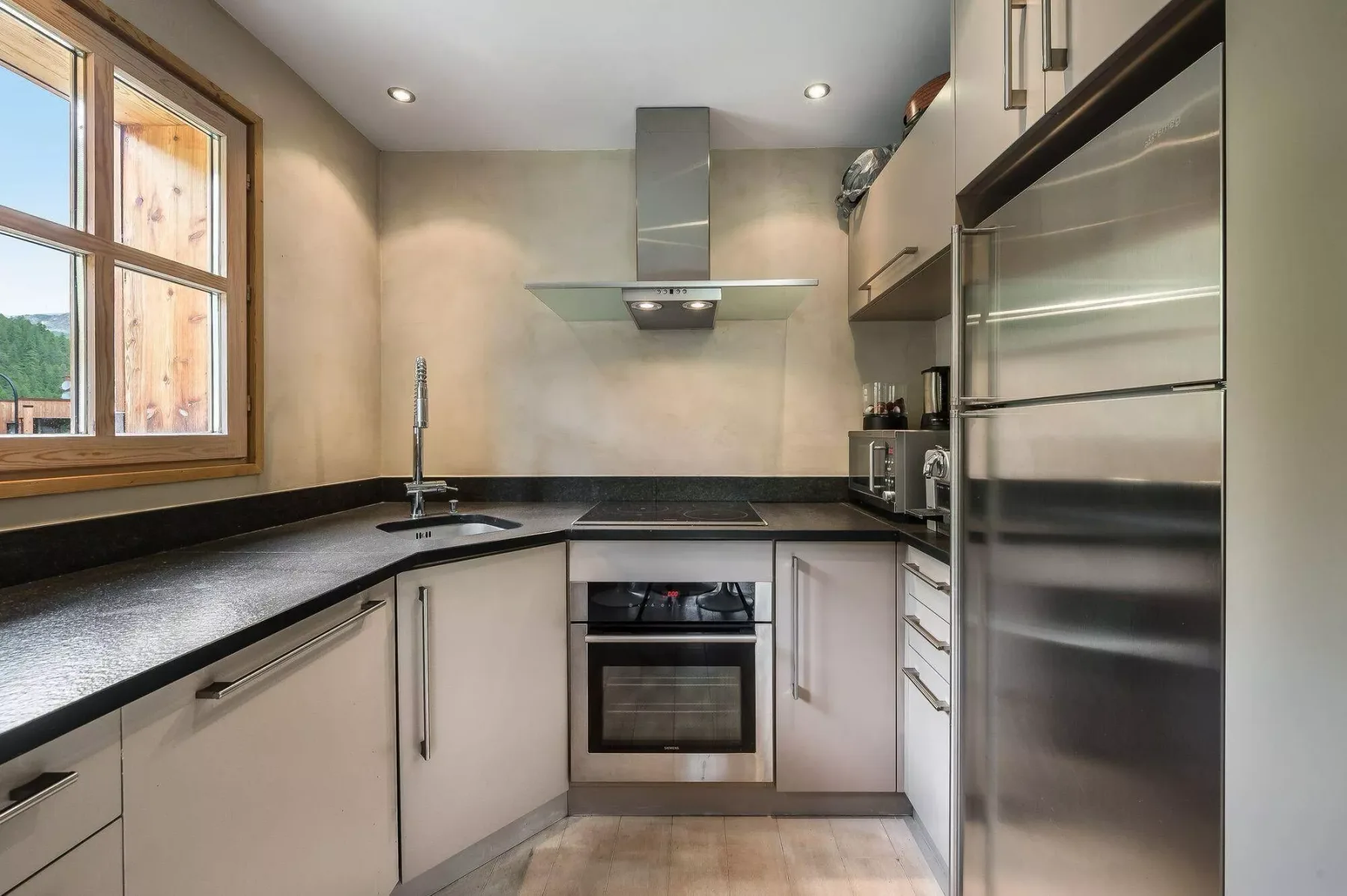 Una cocina moderna con encimeras oscuras, electrodomésticos integrados y una ventana.