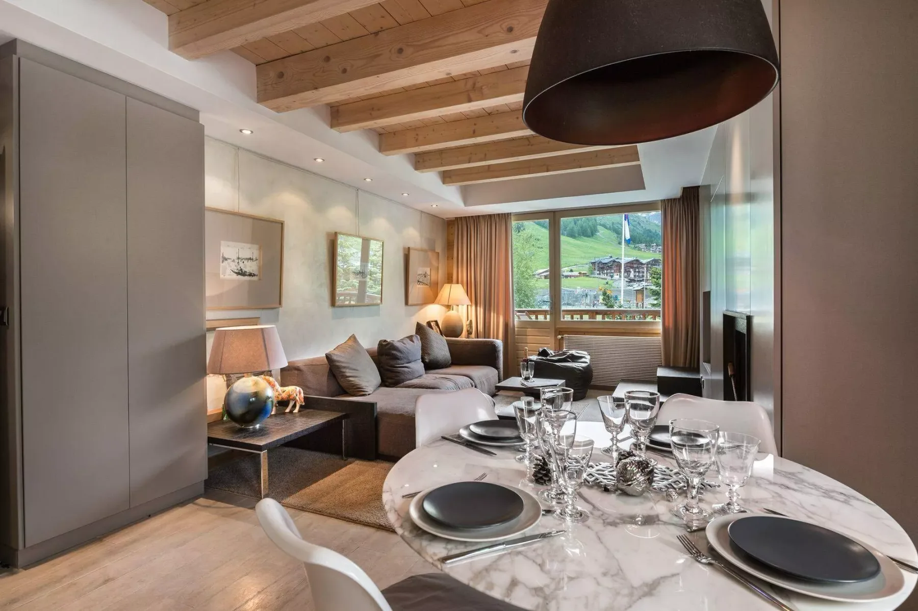 A dining area and living room share a bright space with a set table and large windows.