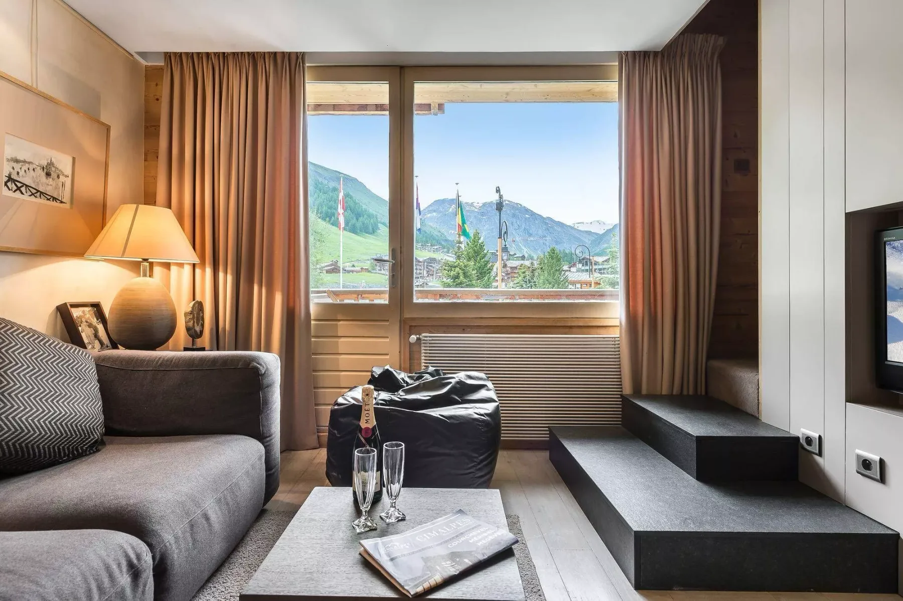A living room with seating beside a large window overlooking a mountain landscape.