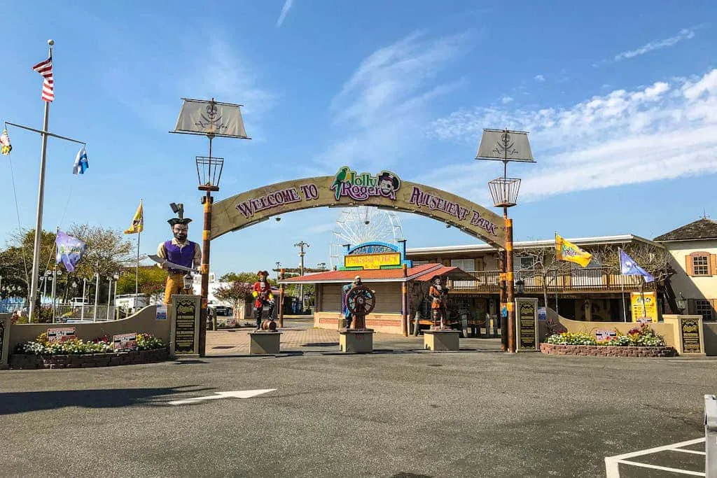 An amusement park entrance with a decorative arch, flags, and colorful attractions.