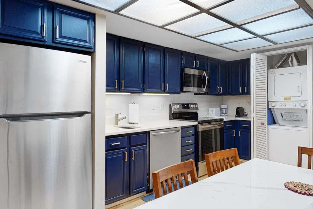A kitchen with dark blue cabinets, stainless steel appliances, and a white island.