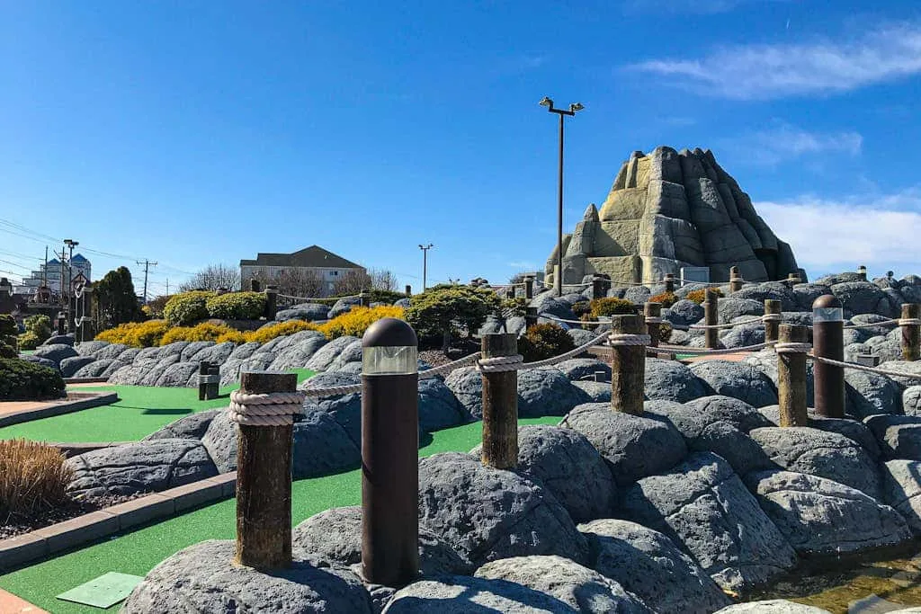An outdoor rocky landscape features a large artificial rock formation and green paths.