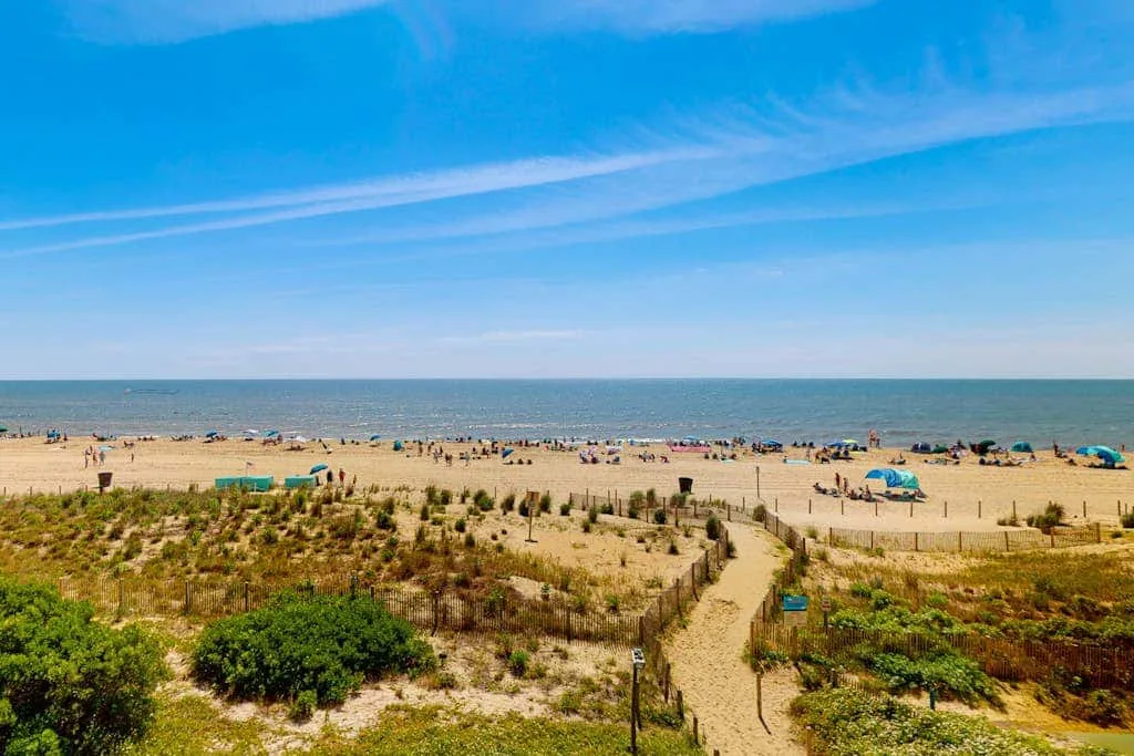 A sandy beach stretches along the sea, with a path through coastal vegetation.