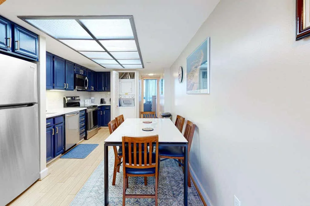 A dining area with a wooden table and chairs beside a blue-cabinet kitchen.