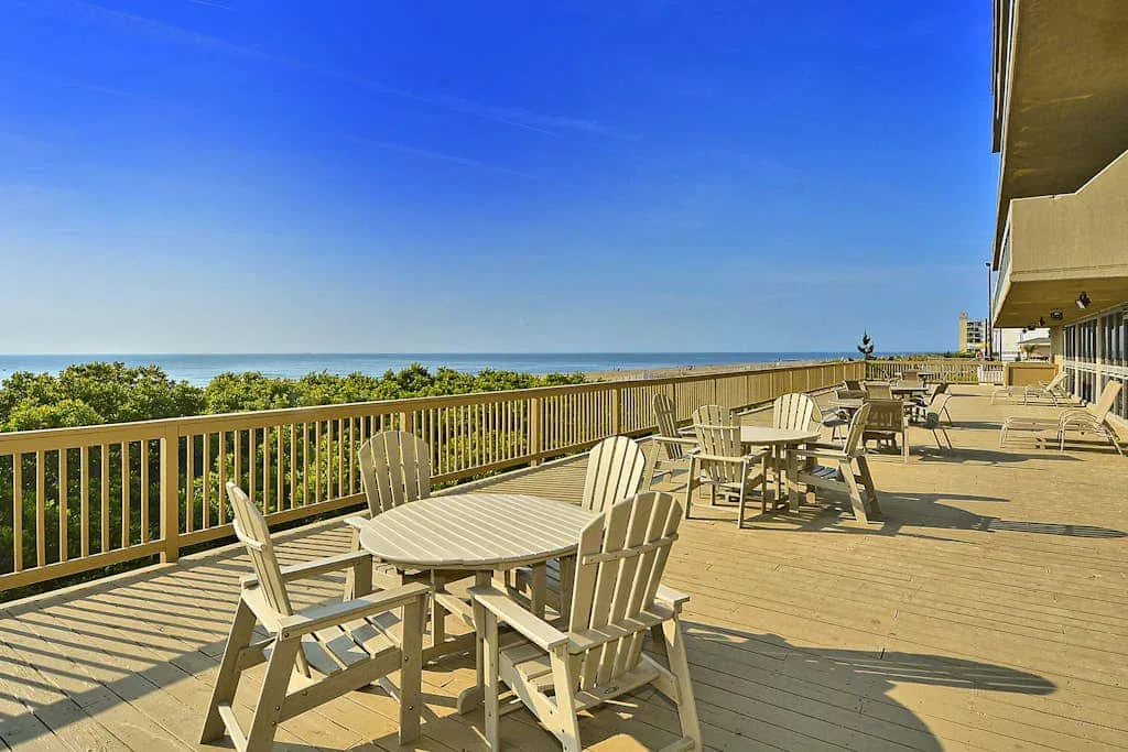 An outdoor deck with seating and tables overlooks the ocean.
