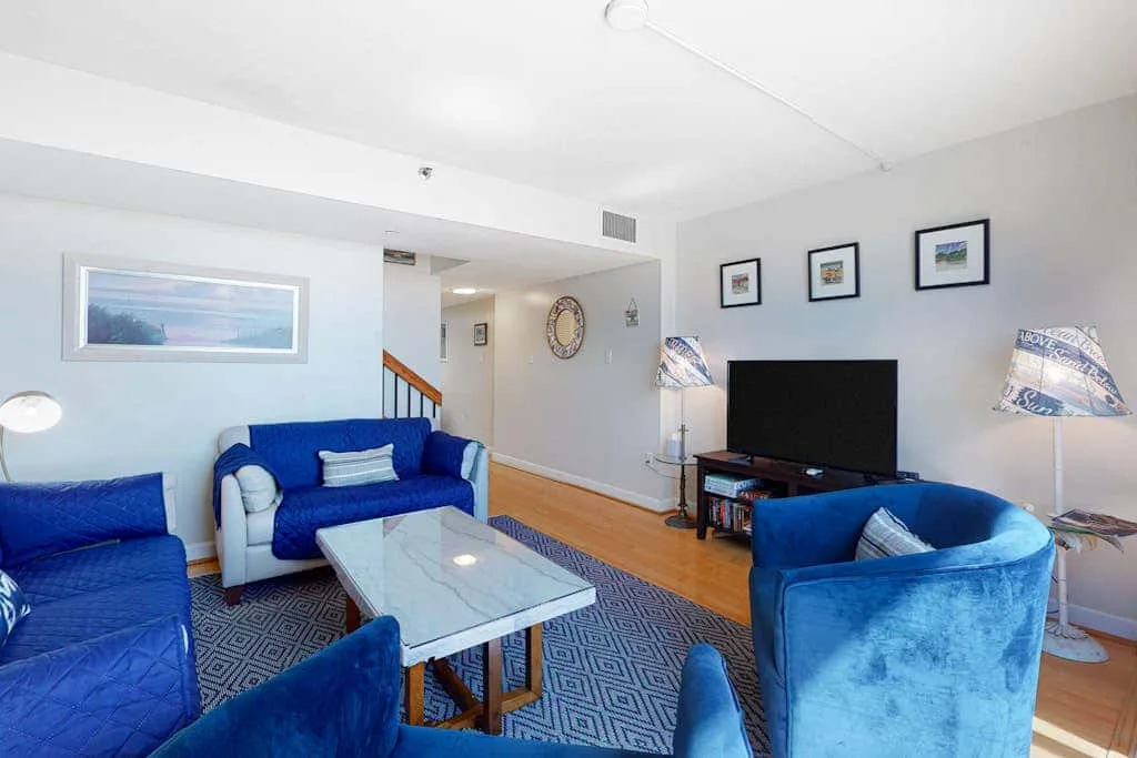 A bright living room with blue seating, a glass coffee table, and a television.