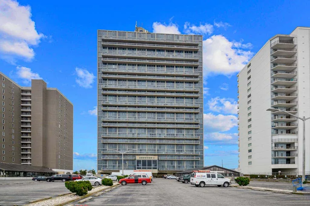 Several high-rise buildings stand beside a paved parking area under a blue sky.
