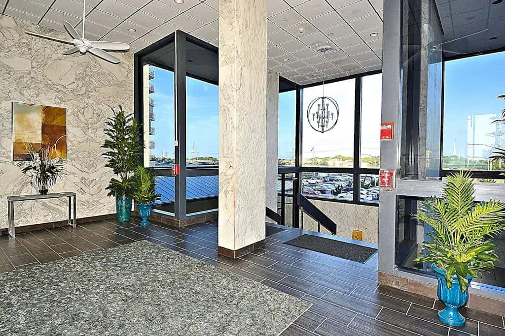 A bright lobby with large windows, tiled flooring, and potted plants.