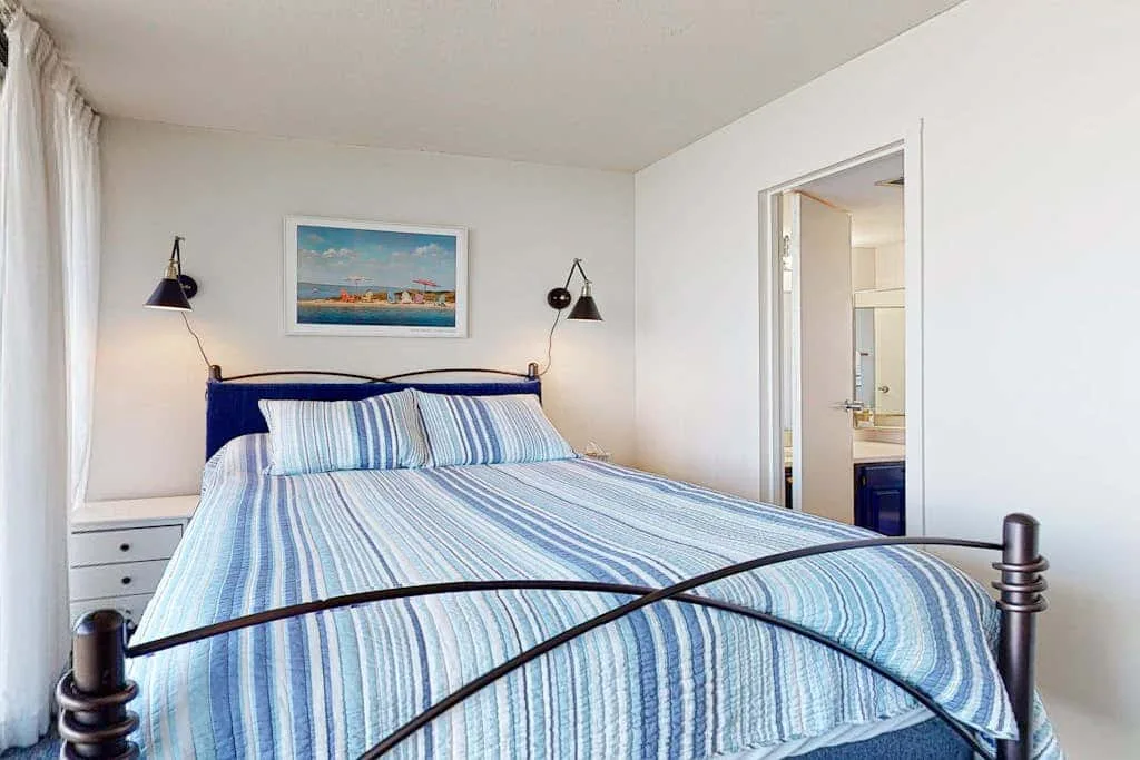 A bedroom with blue-striped bedding and a framed picture above the bed.