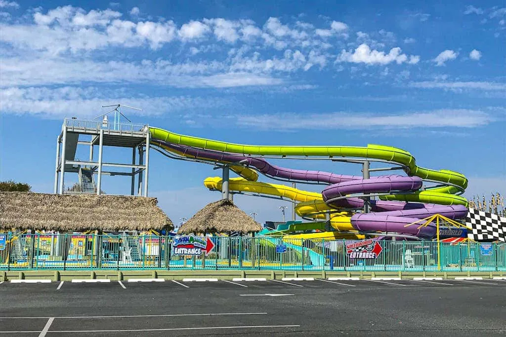 A colorful water park slide complex stands behind a fenced parking area.