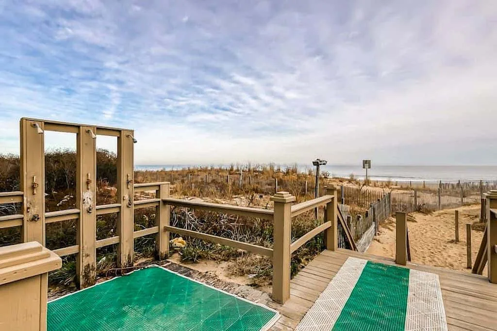 A wooden deck overlooks a sandy beach and coastal dunes.