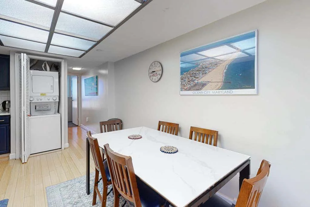 A dining area with a long table and wooden chairs beneath a framed coastal photograph.