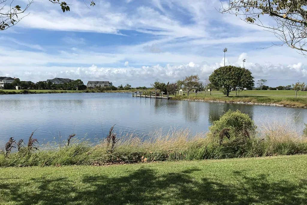 A pond bordered by grass and trees beneath a partly cloudy sky.