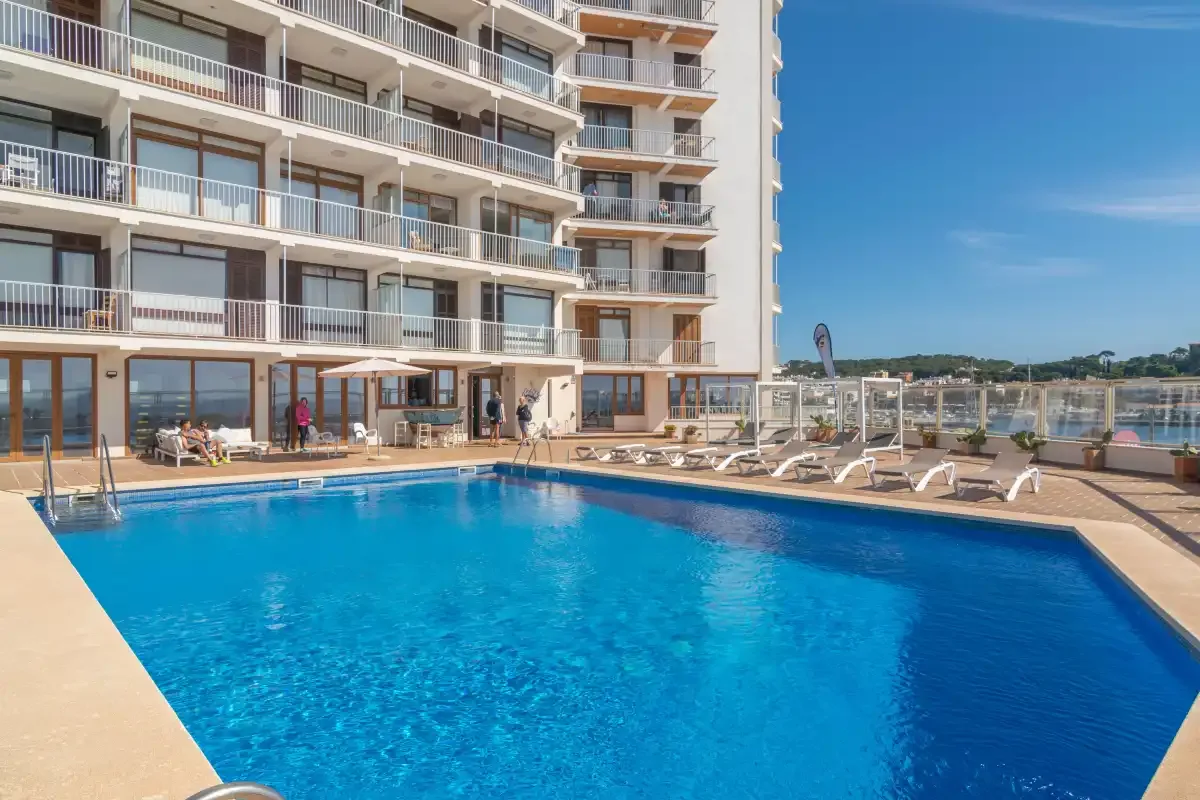 An outdoor swimming pool beside a multi-story building, with lounge chairs along the deck.