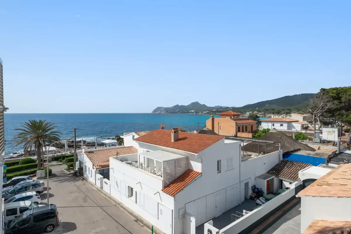 Coastal neighborhood with white buildings, a swimming pool, and the sea beyond.