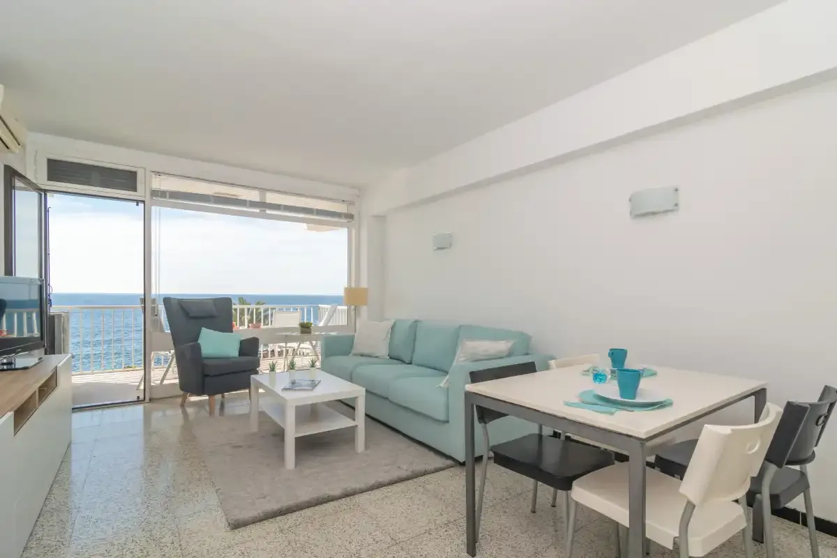 A bright living and dining area with seating beside large windows overlooking the sea.