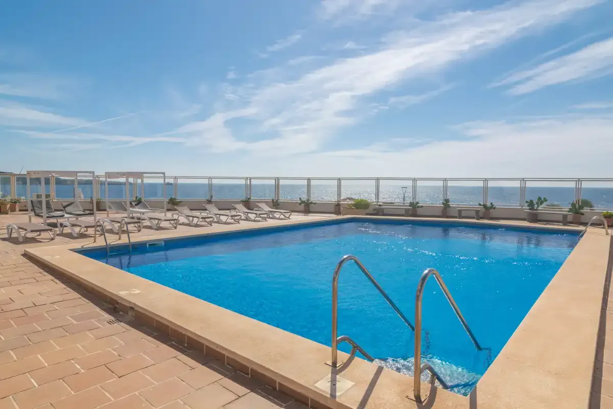 An outdoor swimming pool with lounge seating and a view of the sea.