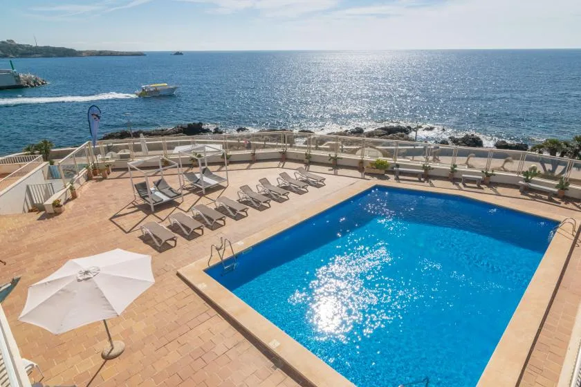 An outdoor swimming pool and sun loungers overlook the sea.