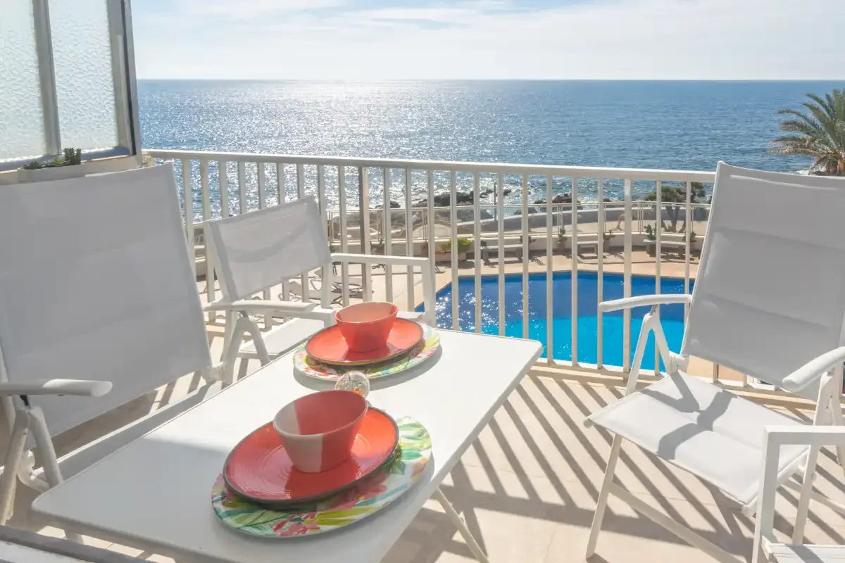 A balcony dining area overlooks a swimming pool and the sea.