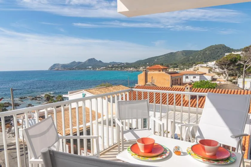 A seaside balcony overlooks the coastline, with outdoor seating and a set table.