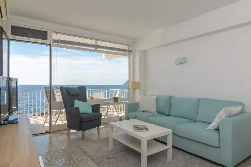 A bright living room opens onto a balcony overlooking the sea.