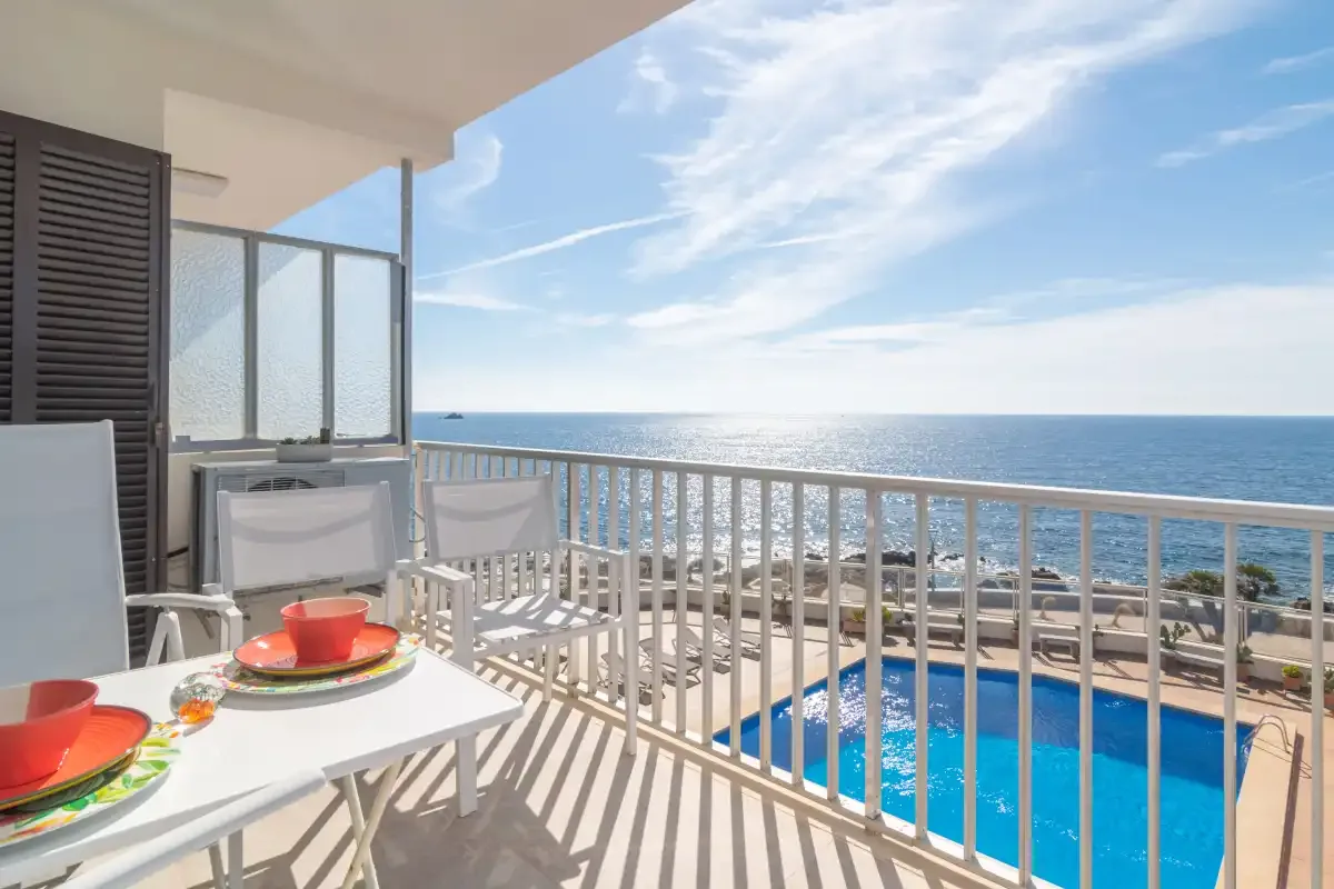 A balcony dining area overlooks a swimming pool and the sea.