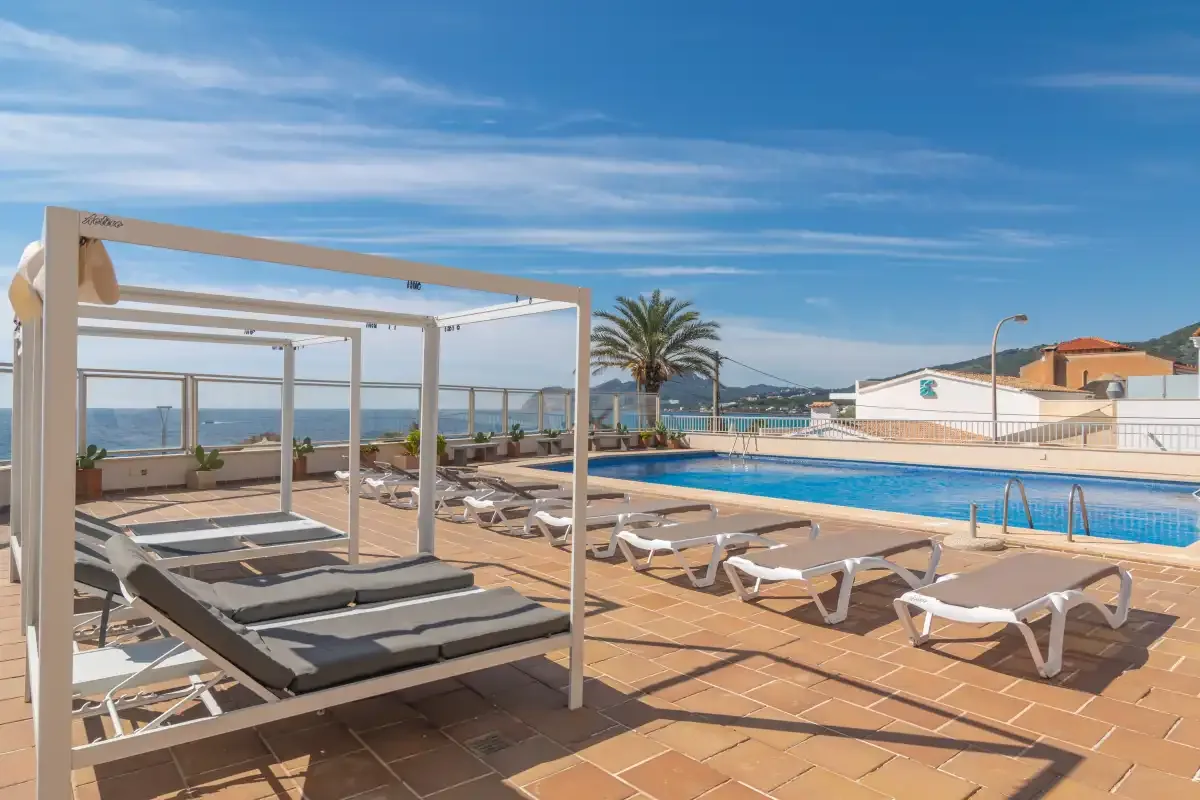 A poolside terrace with lounge seating overlooks the sea.