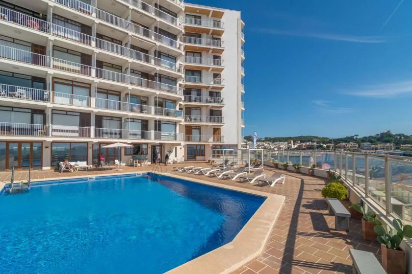 An outdoor swimming pool beside a multi-story building, with lounge seating along the deck.