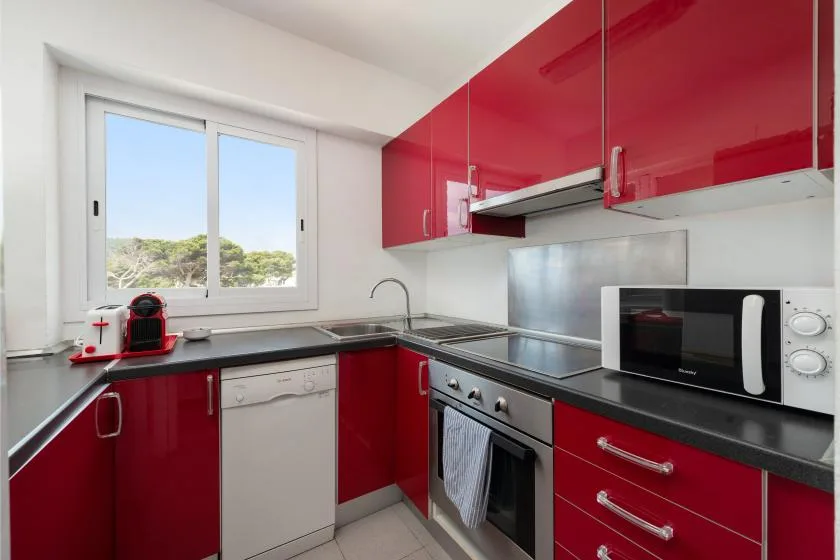 A modern kitchen with red cabinets, dark countertops, and a window.