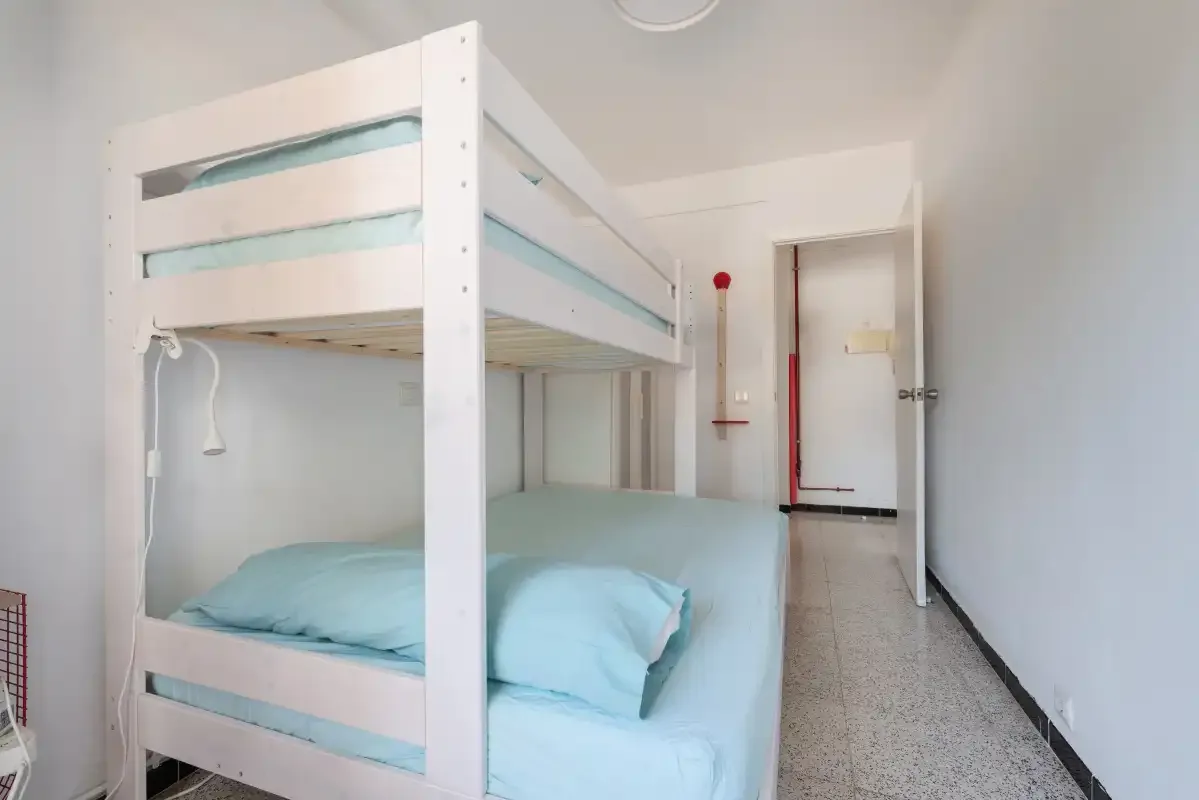 A bunk bed with pale blue bedding stands in a bright room.