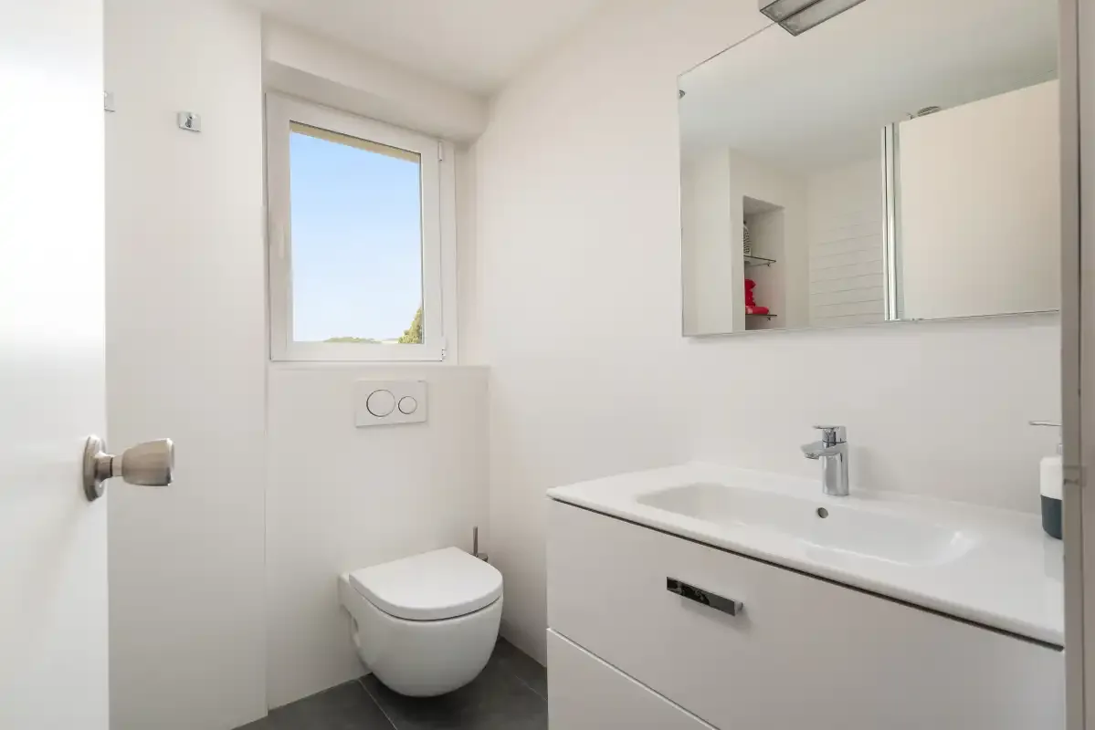 A bright bathroom with a sink, mirror, and toilet.