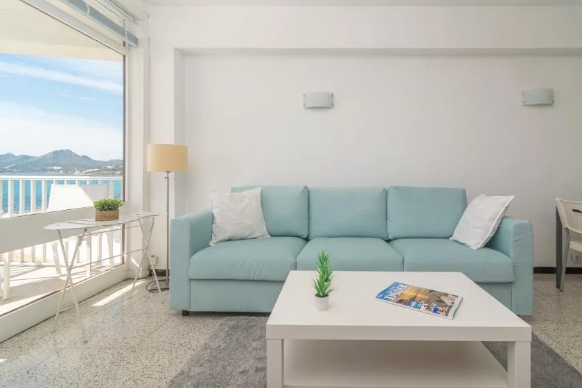A bright living room has a pale blue sofa and a coffee table beside a large window.