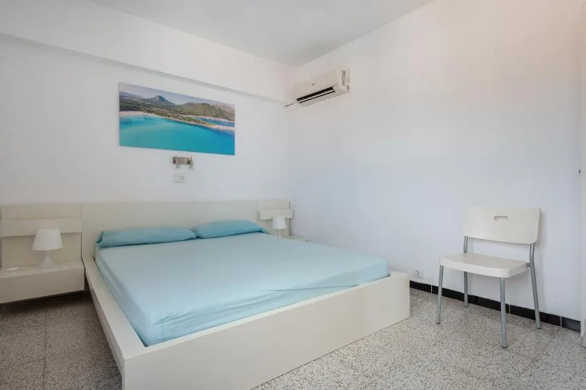 A bedroom with a low bed covered in pale blue bedding and a chair beside it.