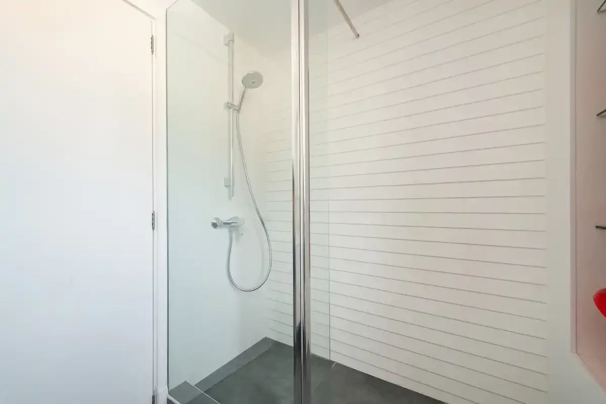 A shower with a handheld showerhead and light horizontal wall paneling.