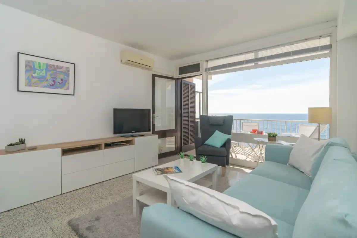 A bright living room opens onto a balcony overlooking the sea.