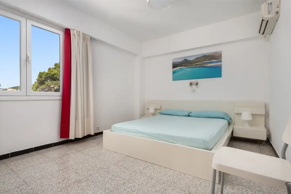 A bright bedroom with a bed beneath a coastal landscape picture.