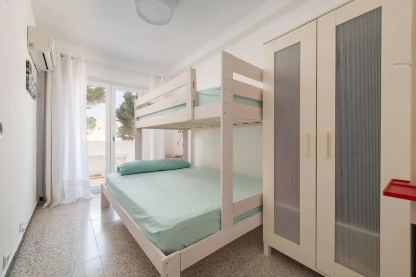 A bedroom with a bunk bed, pale green bedding, and a tall wardrobe.