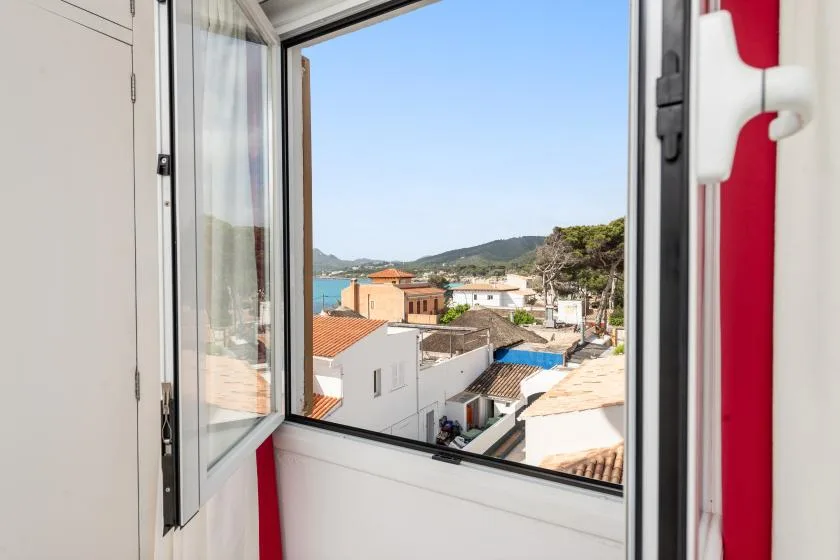 An open window overlooks rooftops, a hillside, and the sea.