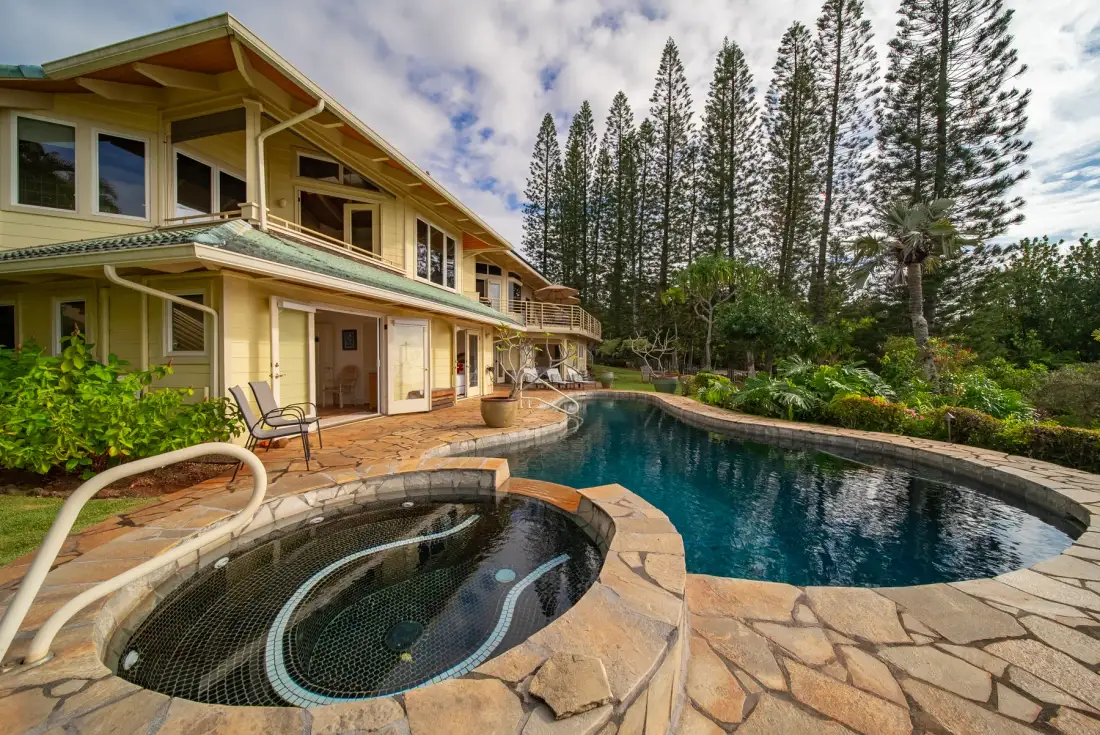 A pool and adjoining spa sit beside a two-story building amid tropical landscaping.